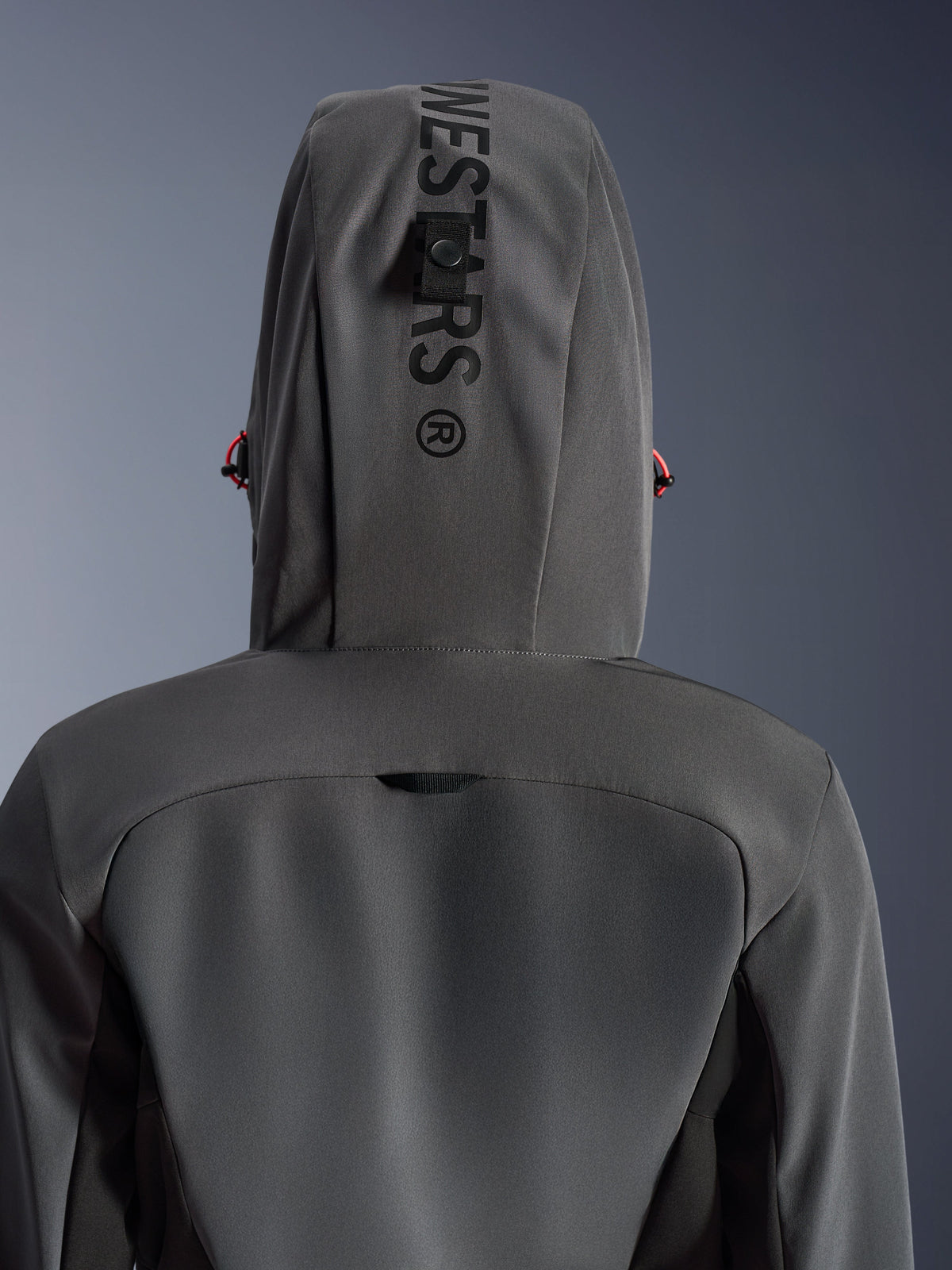 Alpinestars Woman Stella Radium Tech Hoodie, Deep Gray Black, close-up back view showing the hood with vertical branding and management loop, red drawstring accents, durable 3-layer windproof textile construction for urban motorcycle riding.
