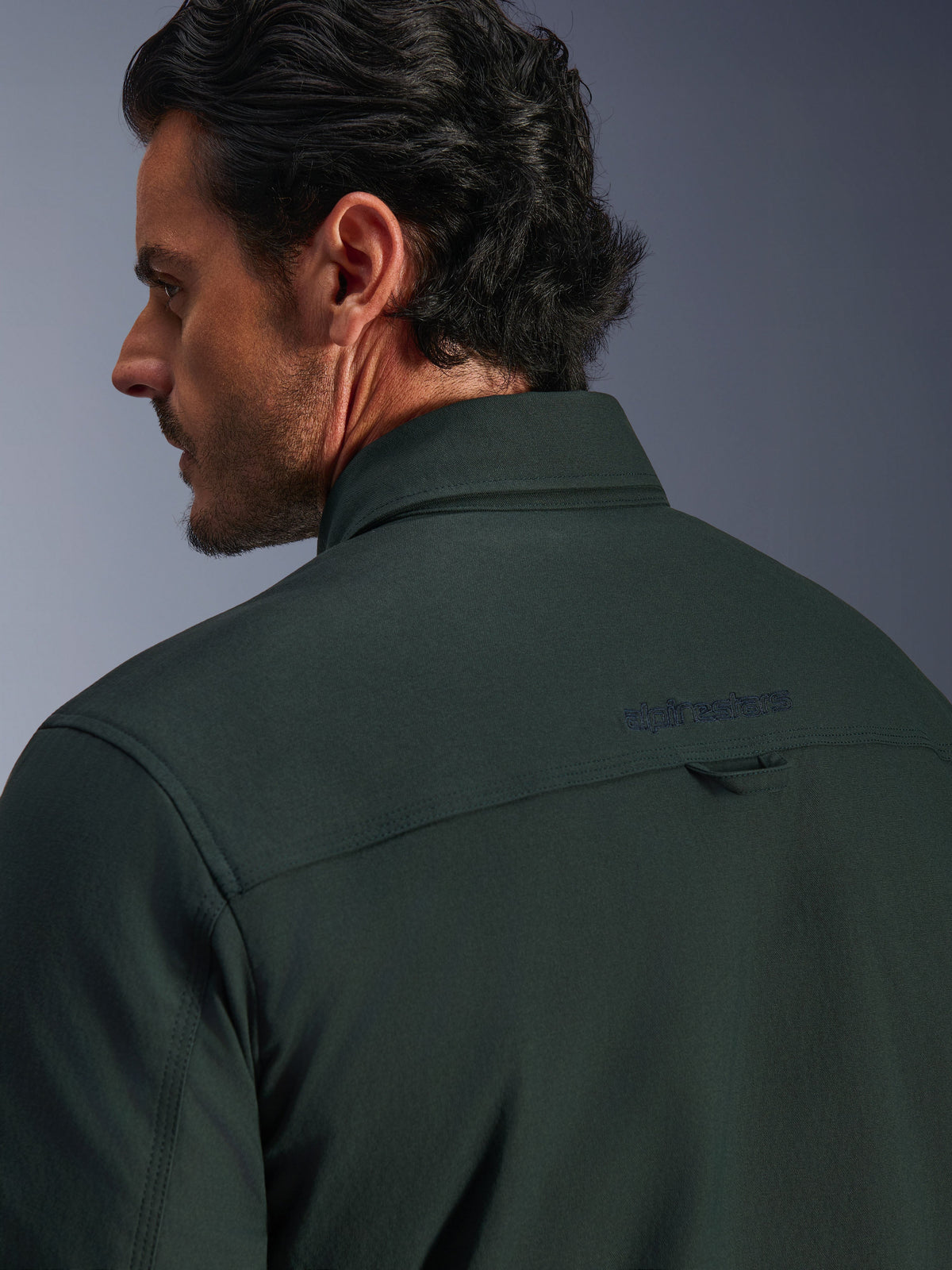 Alpinestars Bryon Water Resistant Overshirt in Dark Emerald green, close-up of the upper back and collar on a male model, featuring an embroidered Alpinestars logo and a small fabric hanging loop, crafted from textured water-resistant waxed canvas for urban motorcycle riding.