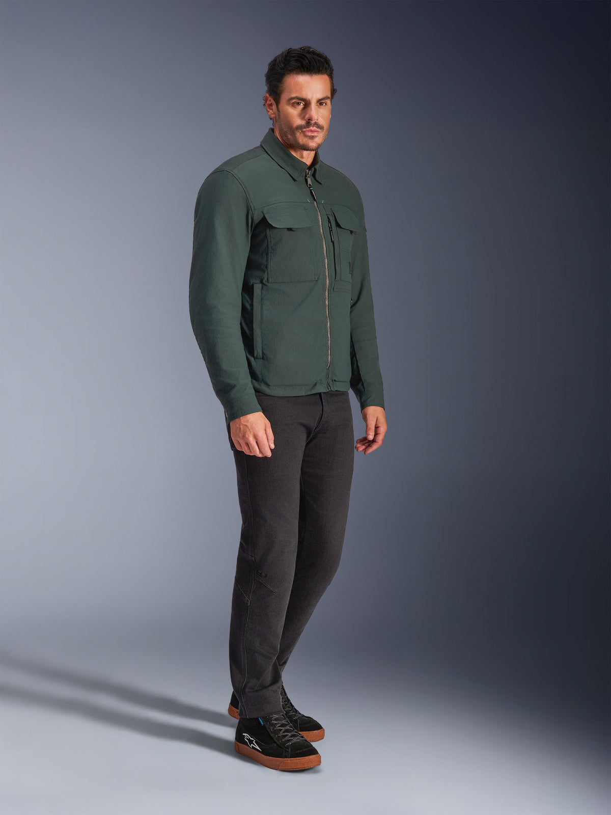 Alpinestars Bryon WR Overshirt, Dark Emerald motorcycle jacket, water-resistant waxed canvas with chest cargo pockets and front zipper, worn by a model with dark trousers and black sneakers, urban contemporary riding gear