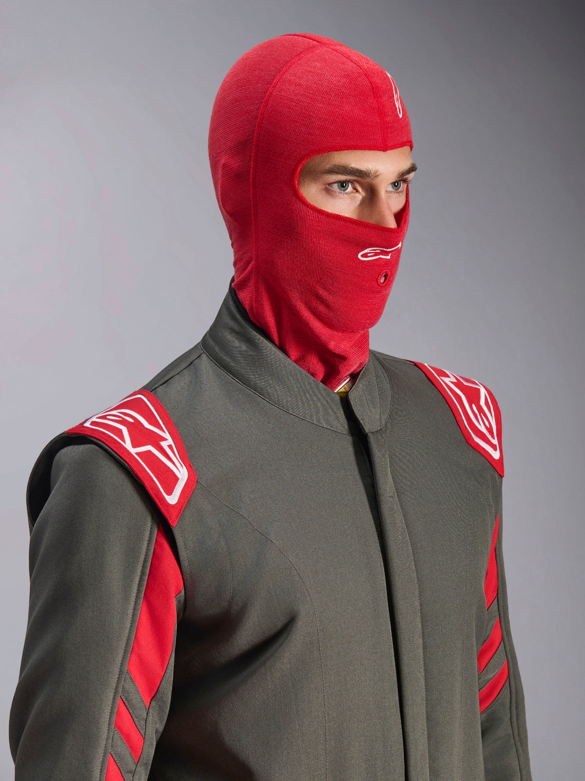 Pasamontañas Alpinestars ZX Evo V3, rojo, usado por un piloto con un traje de carreras gris con detalles rojos y blancos, con un logotipo Astars blanco en la frente y un orificio para tubo de hidratación, capa base resistente al fuego para automovilismo