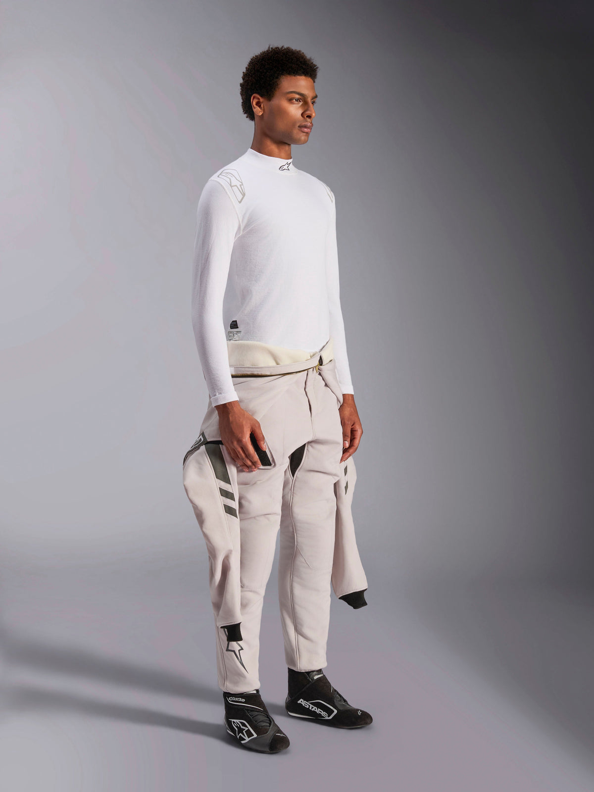Camiseta de manga larga Alpinestars ZX Evo V3, capa base para automovilismo de color blanco y resistente a las llamas, usada por un modelo con un traje de carreras atado a la cintura, capa técnica ligera con cuello alto y detalle del logo