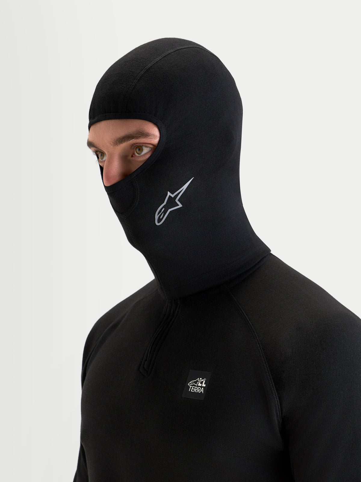 Alpinestars AT-8 Merino Balaclava, black thermal motorcycle balaclava worn by a model, featuring merino wool blend construction, open-face design, and Alpinestars logo detailing for cold-weather adventure riding