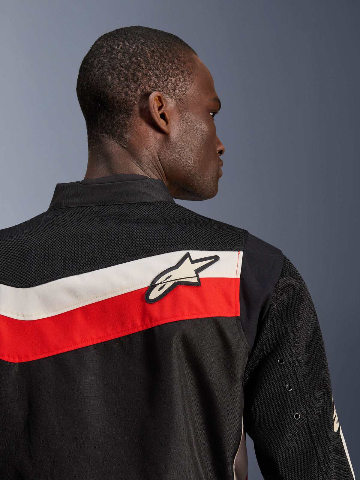 Chaqueta Alpinestars T-Dyno Air, Negro Rojo Brillante Crudo, vista de primer plano de la parte superior de la espalda y el hombro, con franjas horizontales rojas y crudo con un logotipo de Astars blanco, paneles de malla 3D transpirable en el canesú y las mangas, chaqueta de moto textil clásica moderna