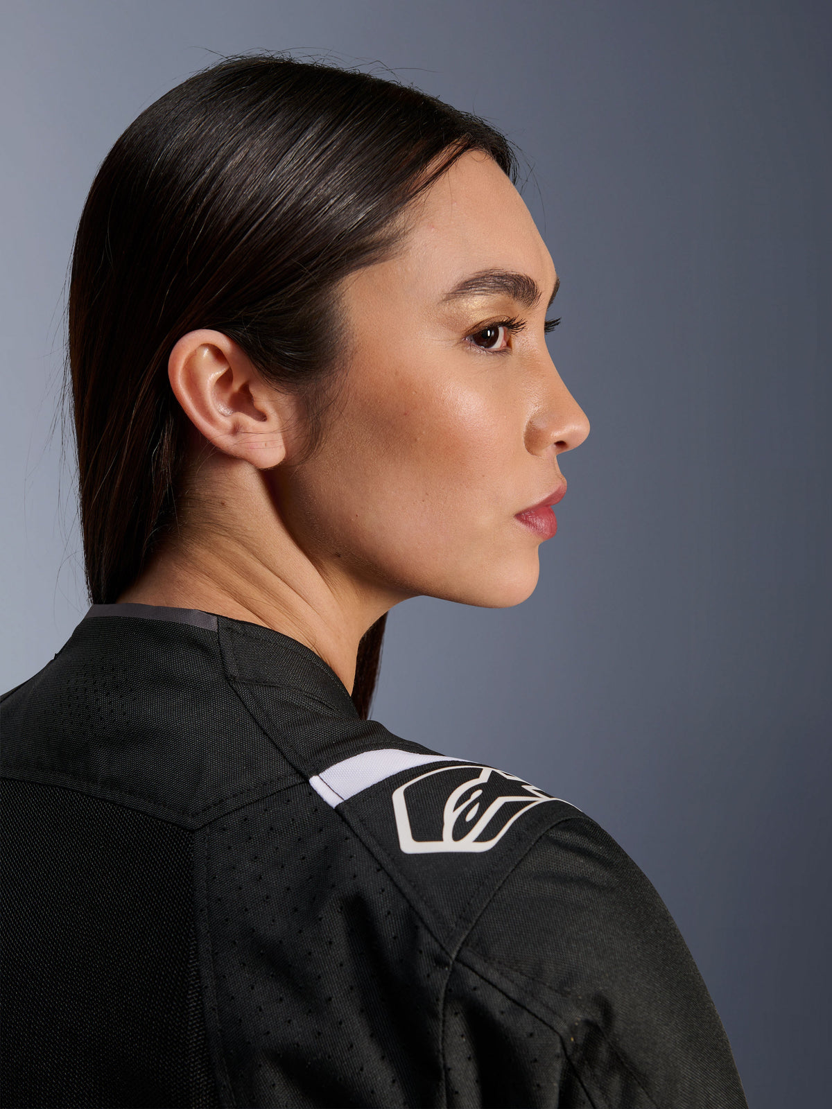 Perfil lateral de una mujer con la chaqueta Alpinestars Stella T-Sps Air V2 en negro y blanco, vista de primer plano centrada en el hombro con logotipo blanco de Alpinestars y construcción de tejido de malla para ventilación.
