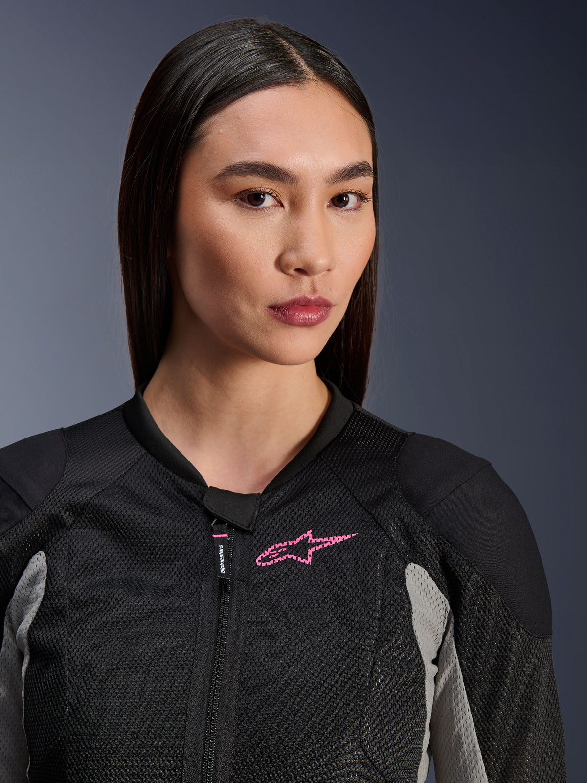 Mujer vistiendo la chaqueta Alpinestars Stella Troop-Air, negro, gris ceniza y rosa flúor, vista de primer plano que resalta la construcción de malla técnica y el logotipo rosa en el pecho, equipamiento de moto urbano con estilo