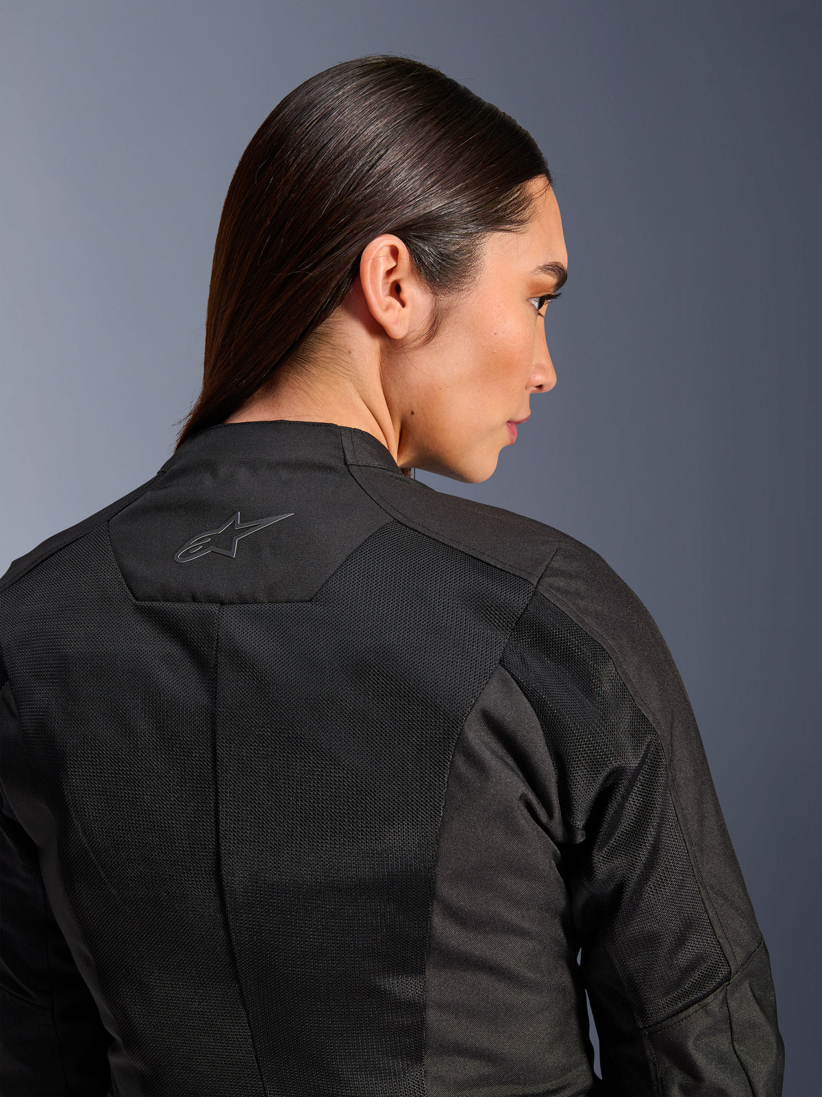 Chaqueta Alpinestars Stella C-1 Air para mujer, chaqueta de moto textil, negra, vista trasera en primer plano que muestra paneles de ventilación de malla técnica y un logotipo de estrella reflectante en la parte superior de la espalda, equipamiento moderno para conducción urbana