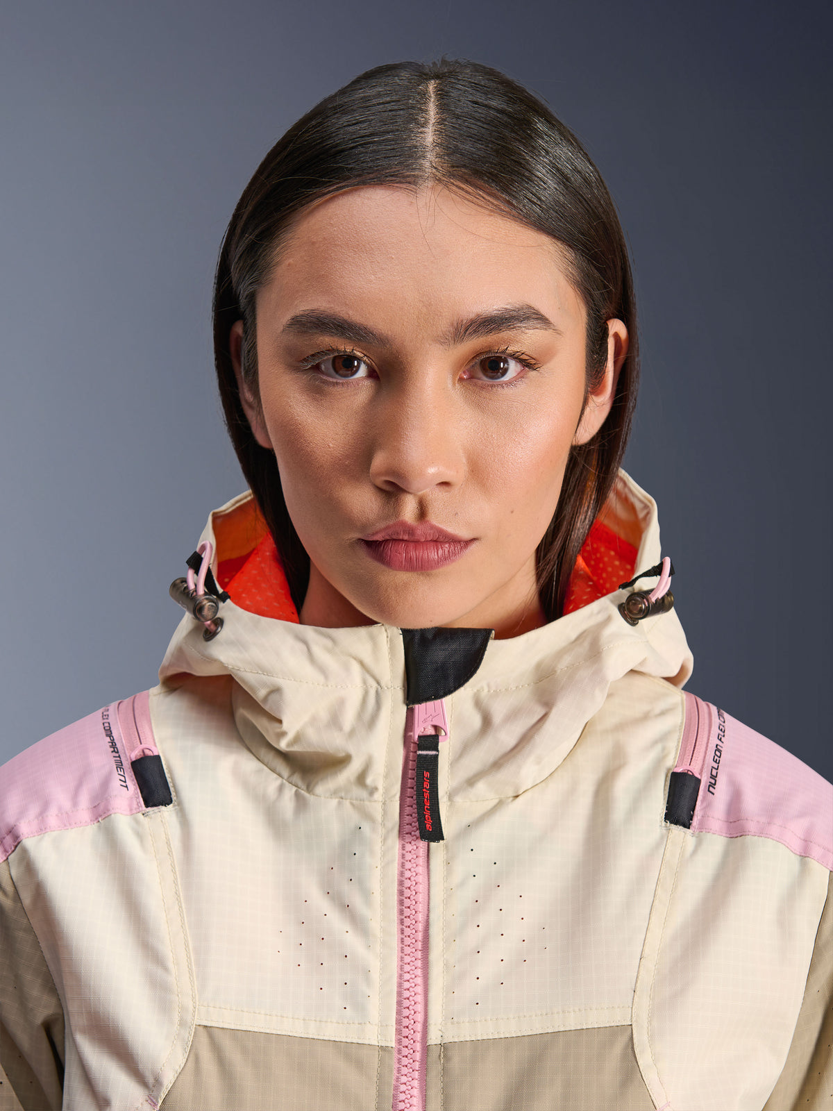 Primer plano de una modelo con la chaqueta Alpinestars Molly Air en Sand Pink Almond, con cuello alto y capucha con forro naranja brillante, cremallera frontal rosa, tejido ripstop con pecho perforado con láser para ventilación, equipamiento de protección para motociclismo urbano