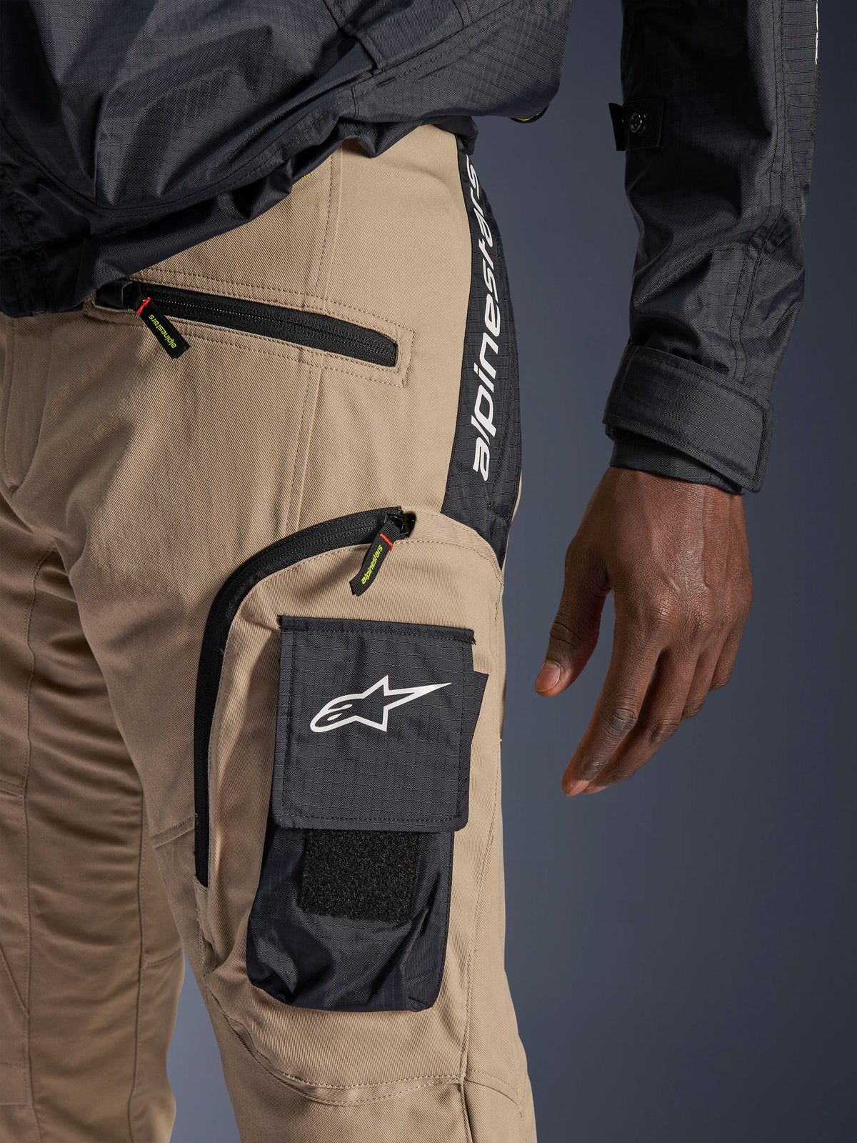 Pantalones Alpinestars Acteon en color arena, vista detallada de la zona de la cadera y el muslo, con un bolsillo cargo lateral negro con el logotipo de la estrella en blanco, bolsillos con cremallera y marca Alpinestars vertical en un panel lateral negro, ropa urbana de motociclismo