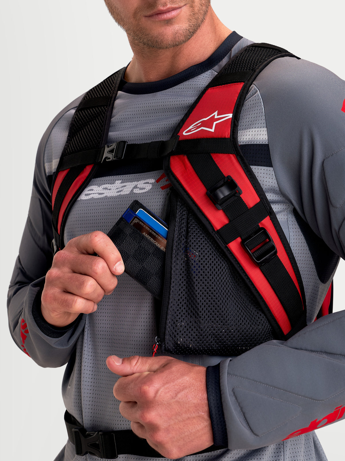 Alpinestars Mochila AT-9, mochila de motocross, negra y rojo brillante, vista en primer plano del sistema de arnés de hombro acolchado y bolsillo de malla con cremallera usado por un modelo