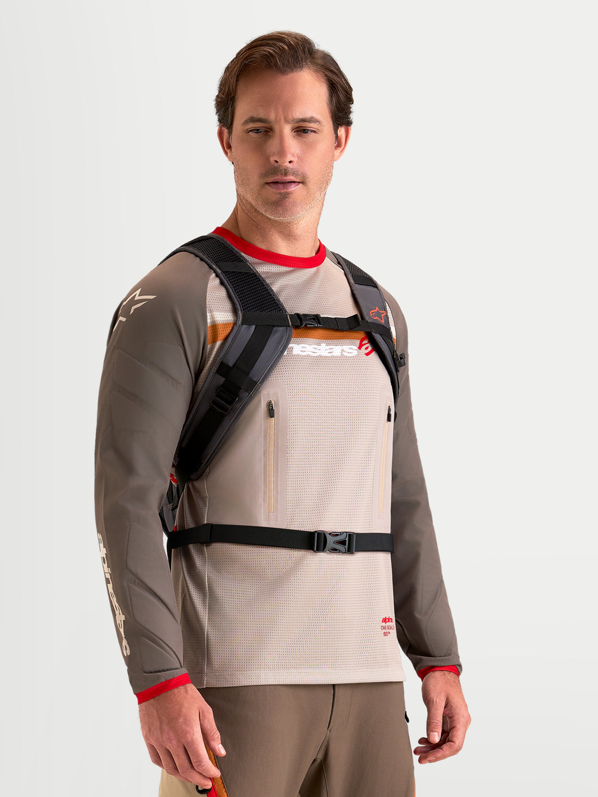 Alpinestars AT-9 Back Pack, mochila de motocross en color marrón y gris oscuro, vista frontal en modelo luciendo el arnés de hombro acolchado y el sistema de cierre con correa de hebilla