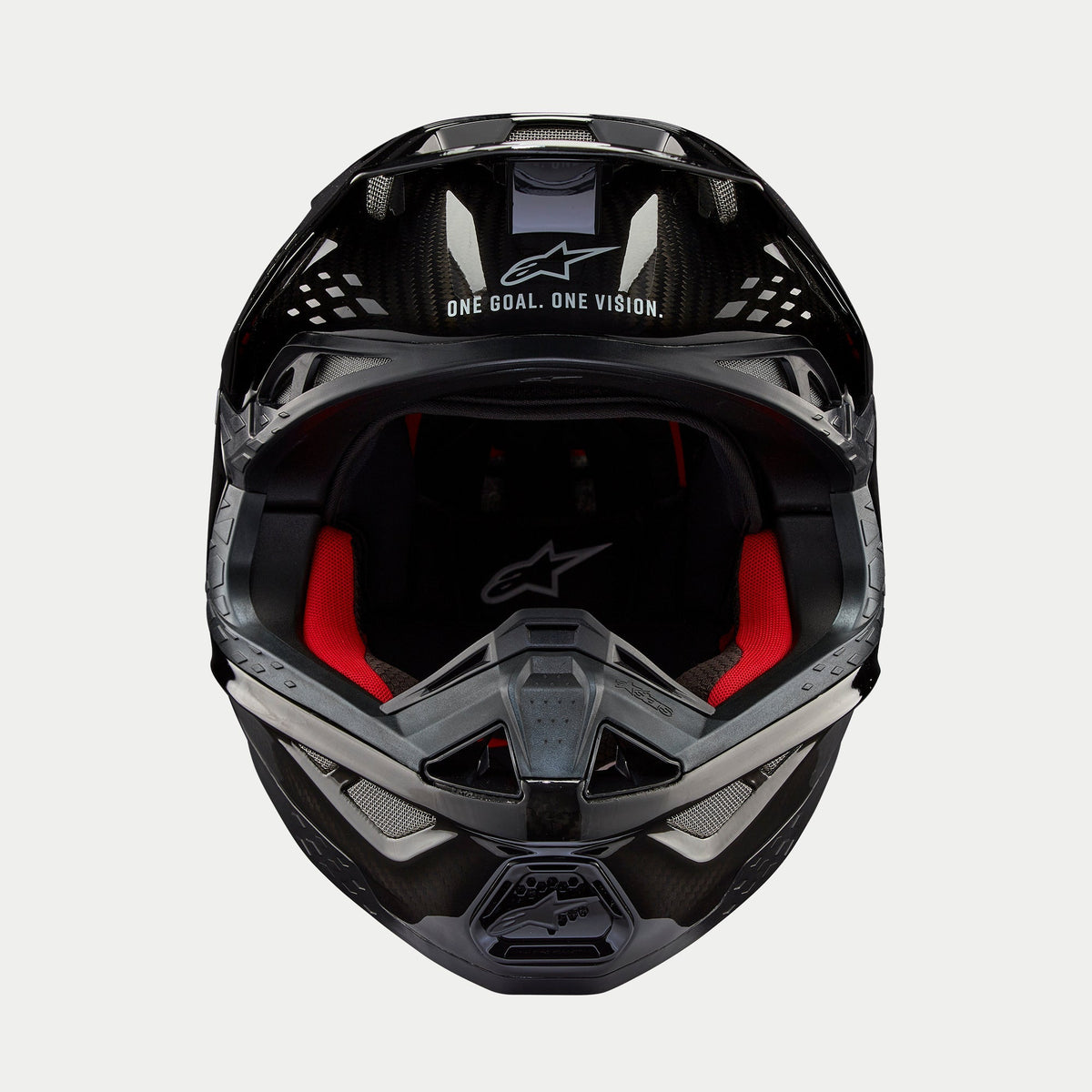 Casco Alpinestars Supertech M10 Solid, casco de motocross, carbono negro brillante, vista frontal que muestra el forro interior rojo, calota de fibra de carbono y el eslogan «ONE GOAL. ONE VISION.» en el área de la visera