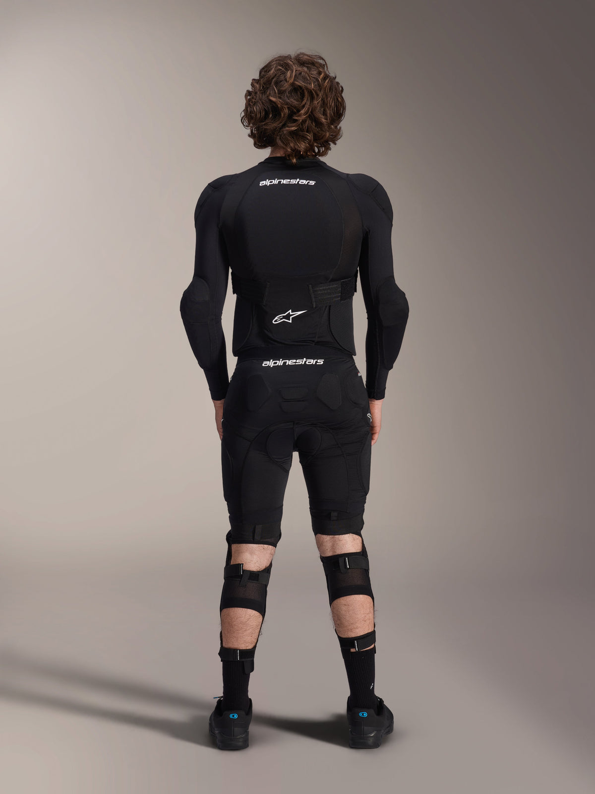 Chaqueta de protección Alpinestars A-Impact Plasma - Manga larga, vista posterior, negra con logotipos blancos de Alpinestars, usada con pantalones cortos de protección y rodilleras para una protección corporal completa de mountain bike