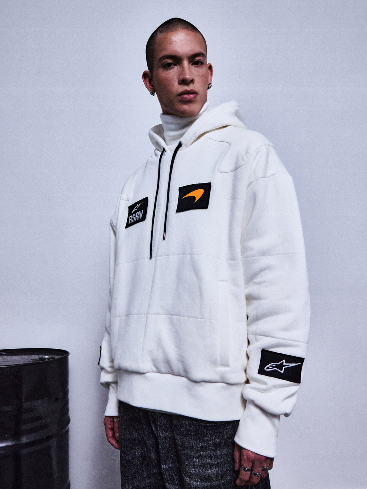 Alpinestars RSRV Rival Hoodie, sudadera blanca con parches negros y naranja, cuello alto incluido, colección streetwear premium, estilo urbano motorsport