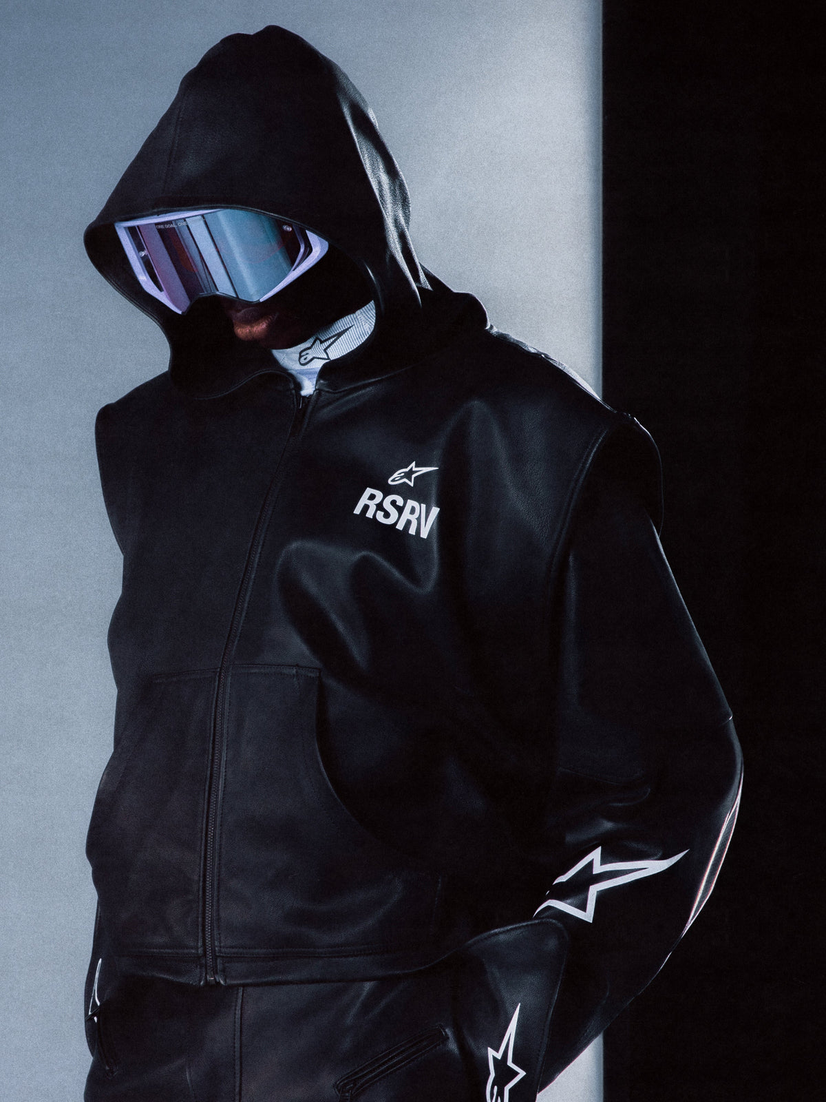 Alpinestars RSRV Axis Leather Hoodie, chaqueta de cuero con capucha negra, logo RSRV y estrella blanca, diseño urbano premium, textura de cuero brillante, estilo futurista moderno