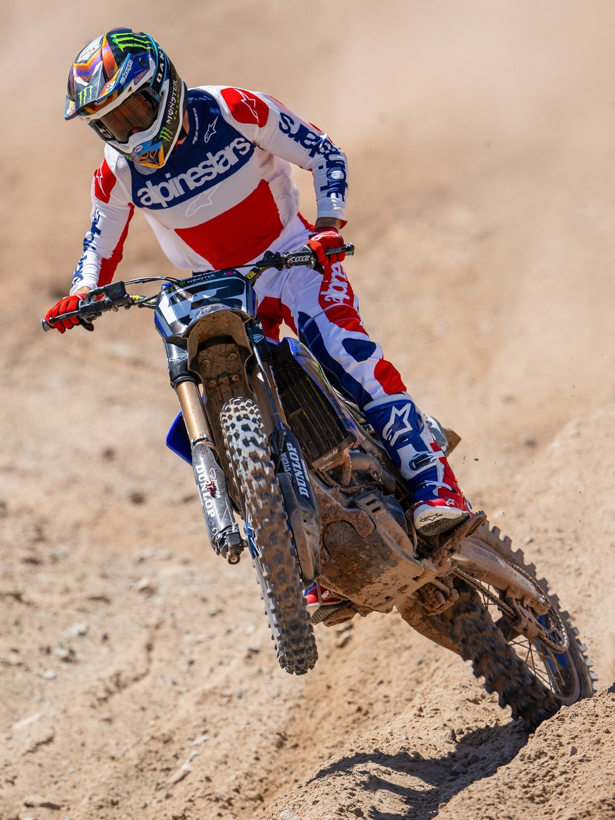 Motocross rider in action on a dirt track, wearing the Limited Edition Techstar Fortitude Jersey in Bright Red White and Blue, coordinated with matching racing pants and boots, featuring bold Alpinestars branding, professional off-road racing apparel