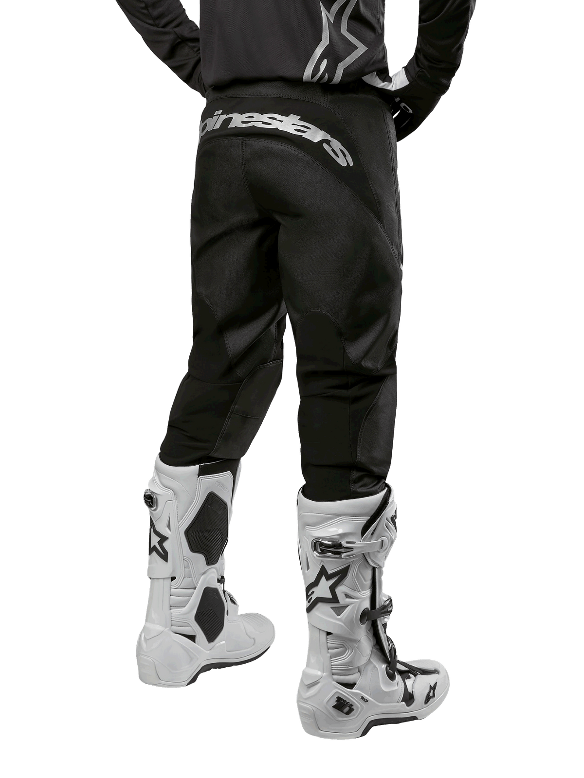 Alpinestars 2024 Fluid Graphite Pants, pantalones de motocross, negro y plata, vista trasera que muestra la marca Alpinestars plateada en el yugo trasero, usados con botas de motocross blancas y negras, diseño textil duradero para conducción fuera de carretera