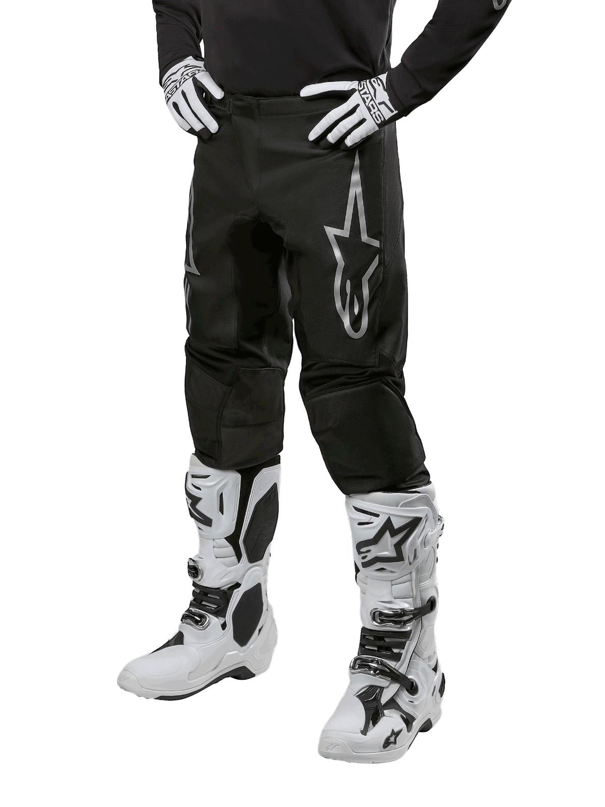Alpinestars 2024 Fluid Graphite Pants, pantalones de motocross, negros y plateados, con un logotipo plateado de Alpinestars en el muslo, mostrados con botas y guantes de motocross blancos, diseñados para carreras de motos fuera de carretera