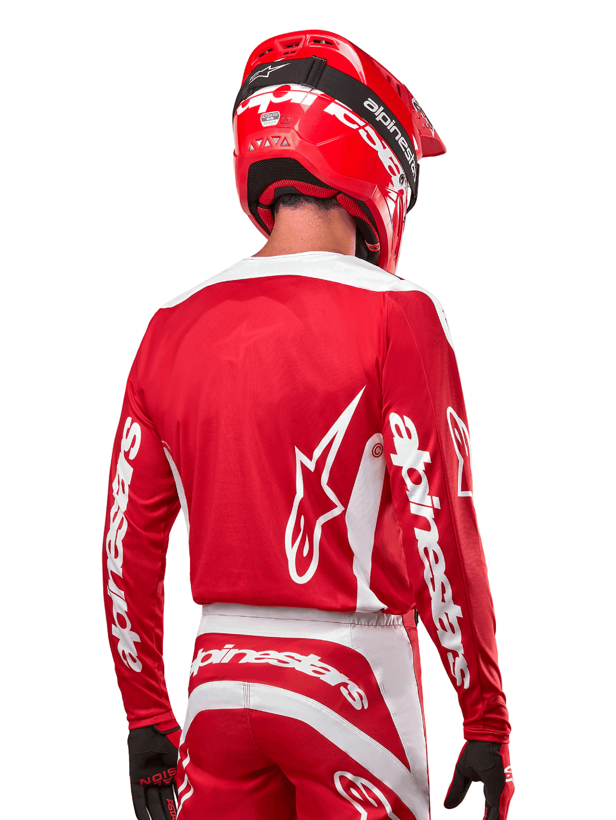 Piloto de motocross con el Jersey Alpinestars 2024 Fluid Lurv, rojo Marte y blanco, vista trasera que muestra el logotipo blanco de Alpinestars en la espalda y la marca en las mangas, combinado con un casco rojo a juego y guantes negros, equipamiento profesional para carreras todoterreno