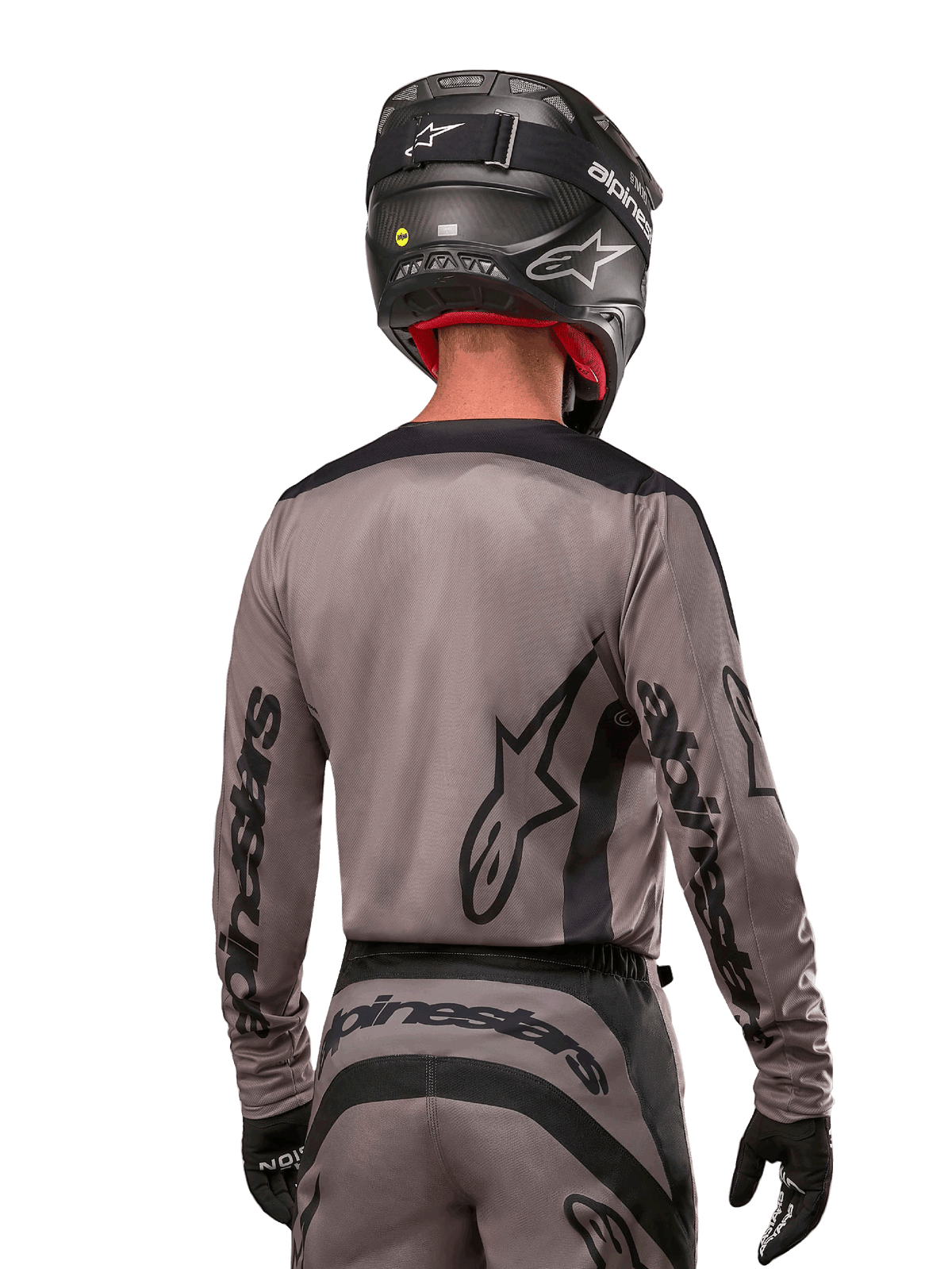 Piloto de motocross visto desde atrás con el jersey Alpinestars 2024 Fluid Lurv en color Mud Black, con logotipos negros de Alpinestars en las mangas y la espalda, combinado con un casco negro y equipamiento a juego para carreras off-road