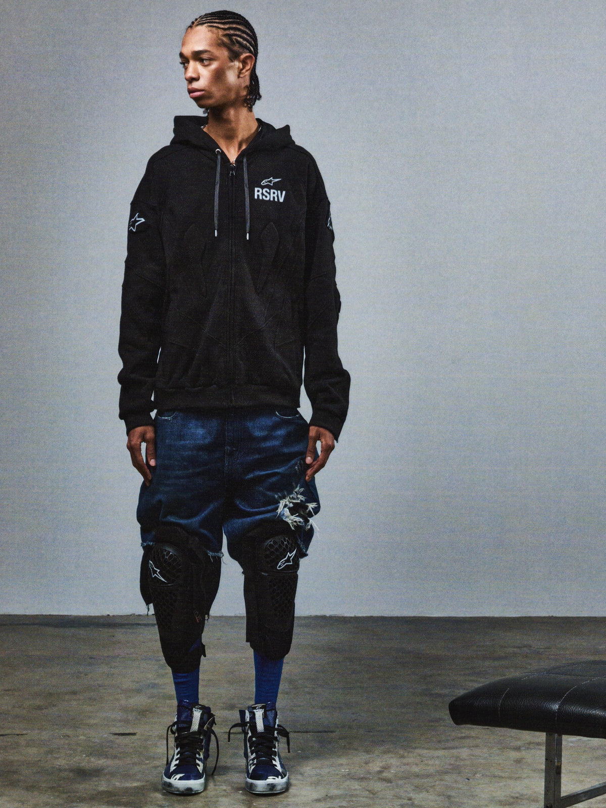 Alpinestars RSRV GP Hoodie, sudadera negra con logo RSRV, estilo urbano de moda, unisex, diseño inspirado en carreras, combinada con shorts de mezclilla desgastados y rodilleras de protección