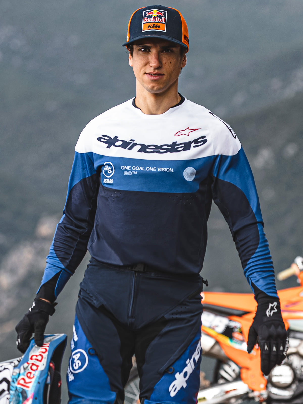 Piloto de motocross vistiendo el jersey Alpinestars Pro-Dura en azul marino, azul brillante y blanco, con el logotipo de Alpinestars y el eslogan 'One Goal. One Vision.', combinado con equipamiento de motocross a juego y una gorra de Red Bull KTM en un entorno al aire libre.