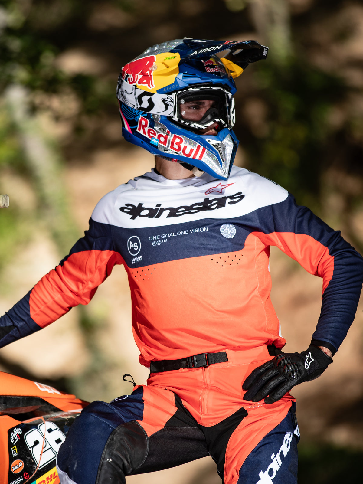 Piloto de motocross con equipamiento Alpinestars Pro-Dura, jersey en azul navy, naranja y blanco con logotipo central de Alpinestars, pantalones Pro-Dura a juego, casco Red Bull y guantes negros, conjunto coordinado para competición profesional de enduro