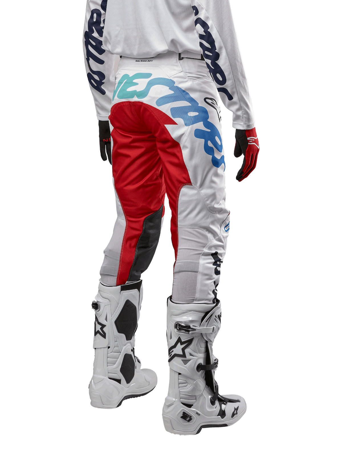 Alpinestars 2024 Racer Hana Pants, pantalones de motocross, blanco multicolor con detalles en rojo y azul, vista posterior que muestra un logotipo grande en el asiento, usados con botas de motocross blancas y negras, diseñados para rendimiento y durabilidad todoterreno