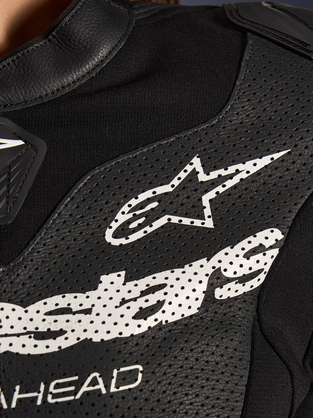 Primer plano del traje de cuero de 2 piezas Alpinestars Stella GP-R7 en color negro, con paneles de cuero perforado, un gran logotipo blanco de Alpinestars en el pecho y secciones de tejido elástico transpirable.