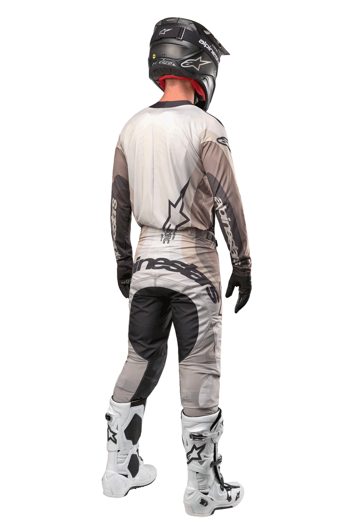 Pantalones Alpinestars Techstar Pneuma 2024, pantalones de motocross, arena oscura y gris polvo de hierro, vista trasera usada por un piloto con jersey a juego, botas blancas y negras y casco negro, con un llamativo logotipo de Alpinestars en el asiento y paneles oscuros reforzados.