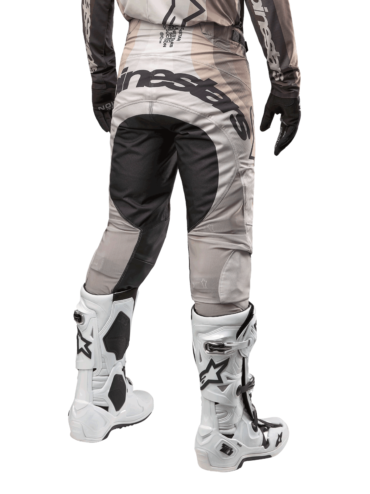 Pantalones Alpinestars Techstar Pneuma 2024, pantalones de motocross, color arena oscura y gris, vista trasera desde la cintura para abajo, logotipo negro de Alpinestars en el asiento, usados con botas de motocross blancas y negras y guantes negros, diseño duradero para competición off-road