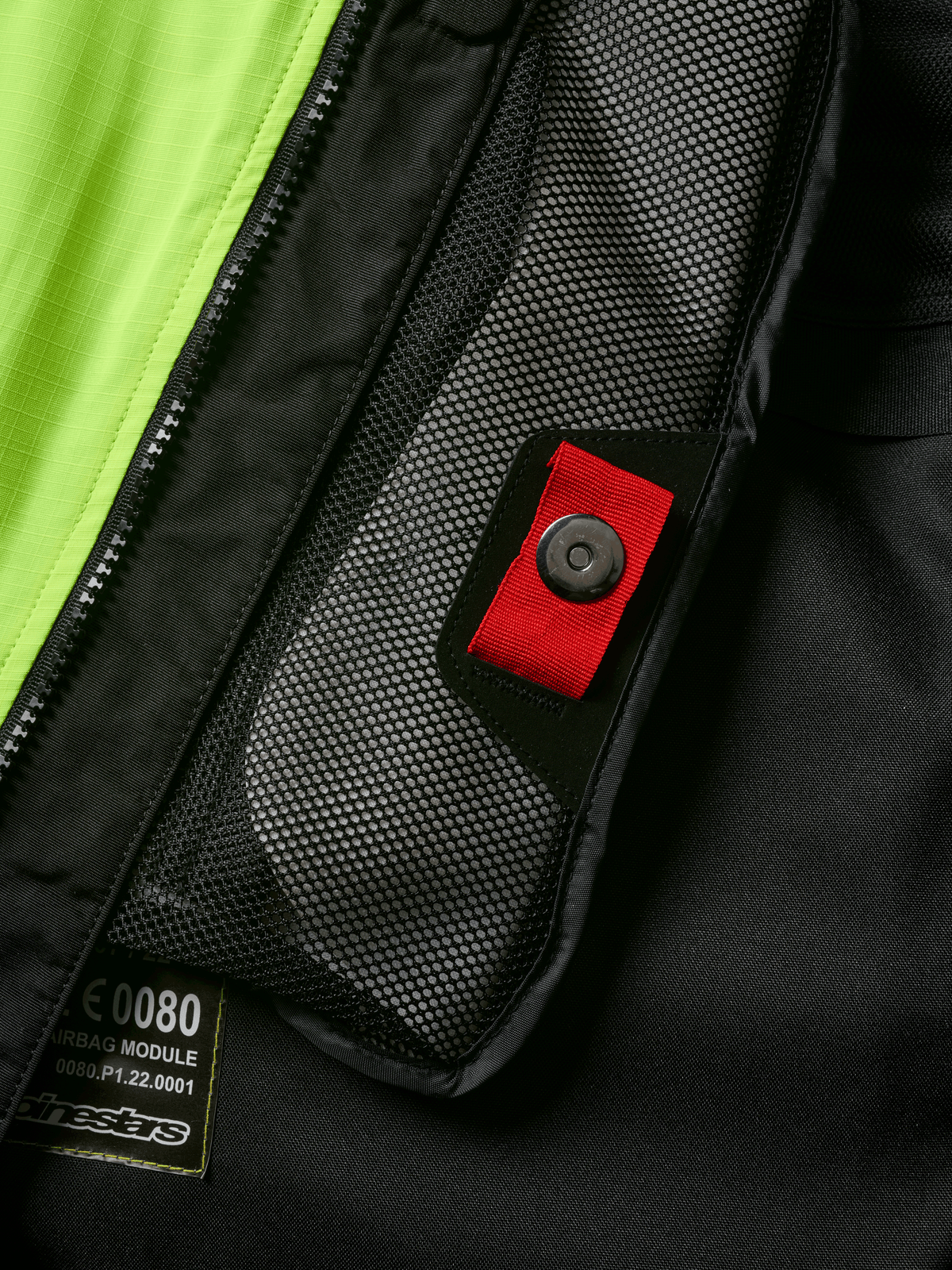 Detalle del sistema Alpinestars Tech-Air® 3 V2, primer plano del bolsillo interno de malla con tirador rojo y cierre de presión, panel amarillo flúor vibrante, construcción textil negra que muestra la etiqueta del módulo de airbag y la cremallera