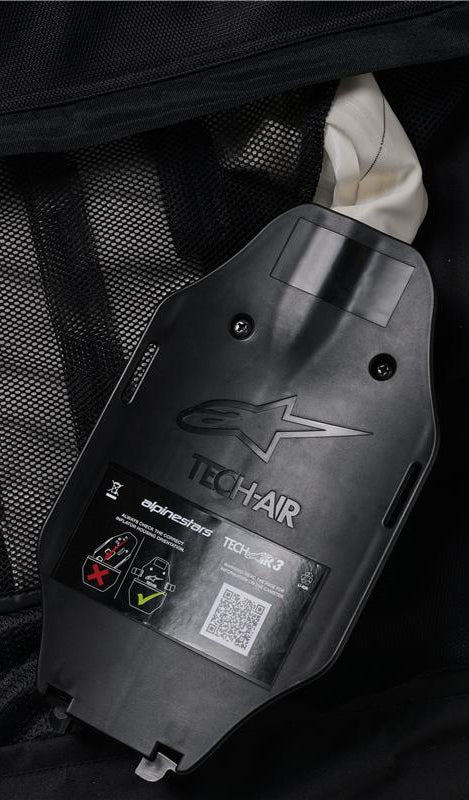 Sistema Alpinestars Tech-Air 3 V2, vista interna del inflador de gas y la carcasa de la ECU, plástico negro con logotipo en relieve, etiqueta de seguridad con código QR y diagramas de instalación, forro interior de malla negra, detalle del sistema de airbag autónomo reparable por el usuario