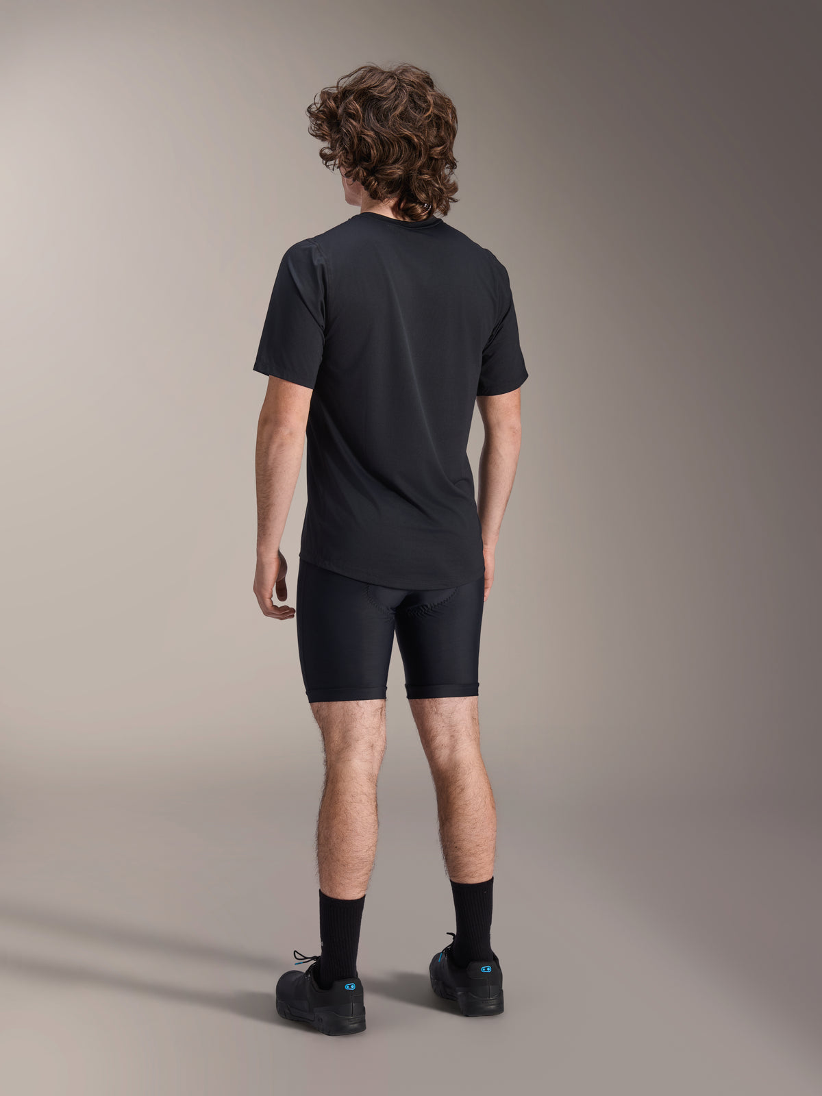 Alpinestars A-Dura Liner Shorts, shorts interiores de ciclismo negros, vista trasera en modelo, tejido elástico ajustado con costuras de acolchado de chamois visibles, combinados con una camiseta negra y zapatillas de ciclismo, ropa de ciclismo de montaña