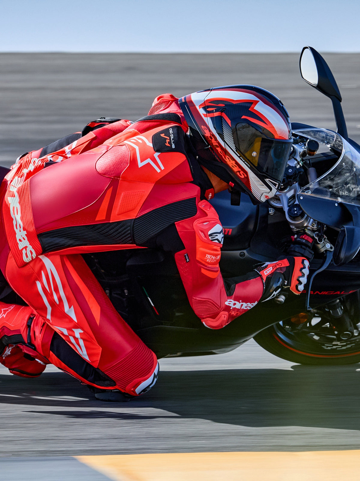 Alpinestars GP Plus V4 Sprint 1PC, mono de cuero rojo fluo y blanco, preparado para Tech-Air, piloto inclinándose en curva.