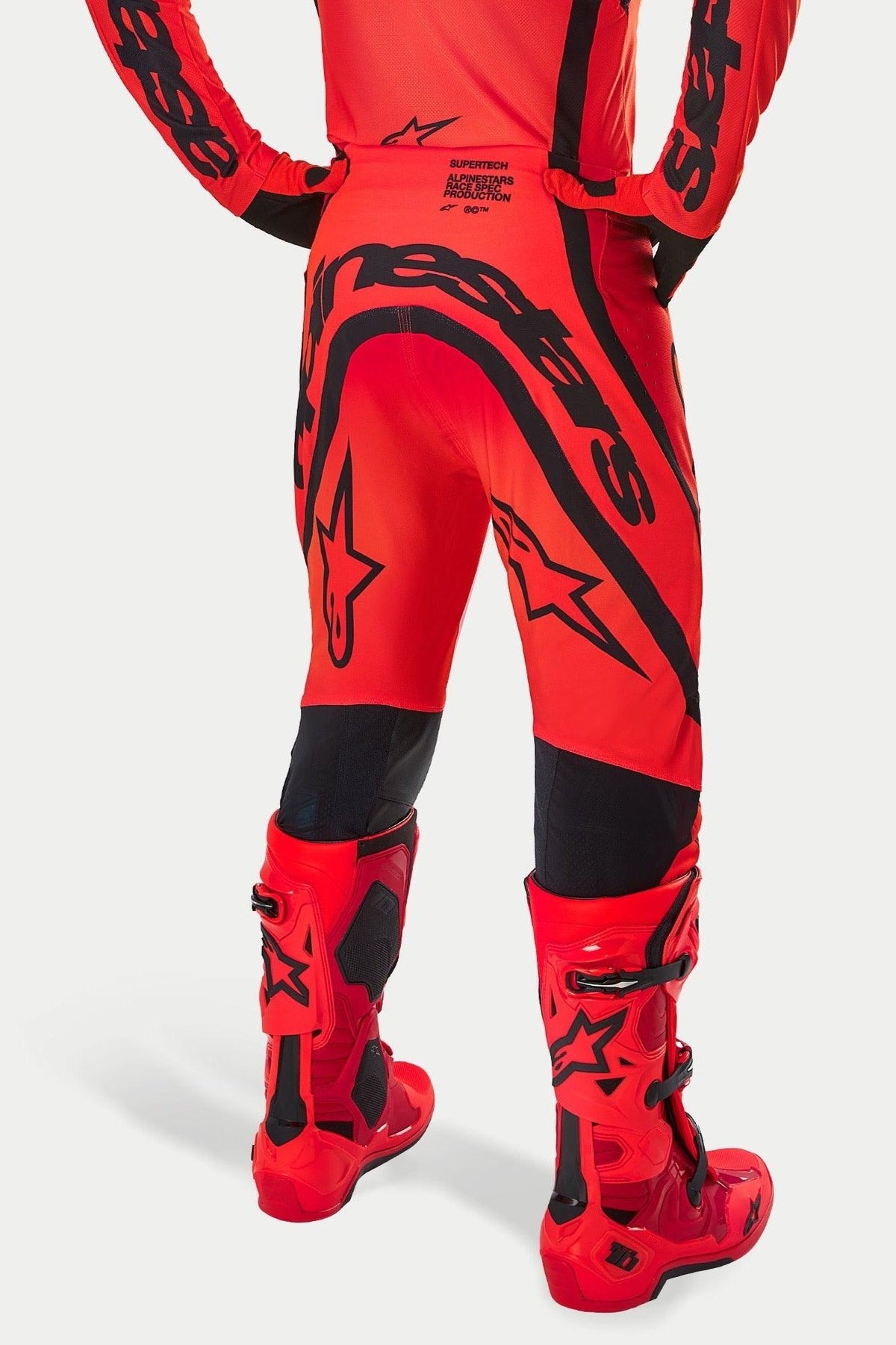 Pantalones Alpinestars Supertech Ember LE, pantalones de motocross en rojo flúor, rojo brillante y negro, vista trasera con gran logotipo negro en el asiento y detalles de estrellas, combinados con botas de motocross rojas a juego, equipamiento de carreras profesional para rendimiento todoterreno