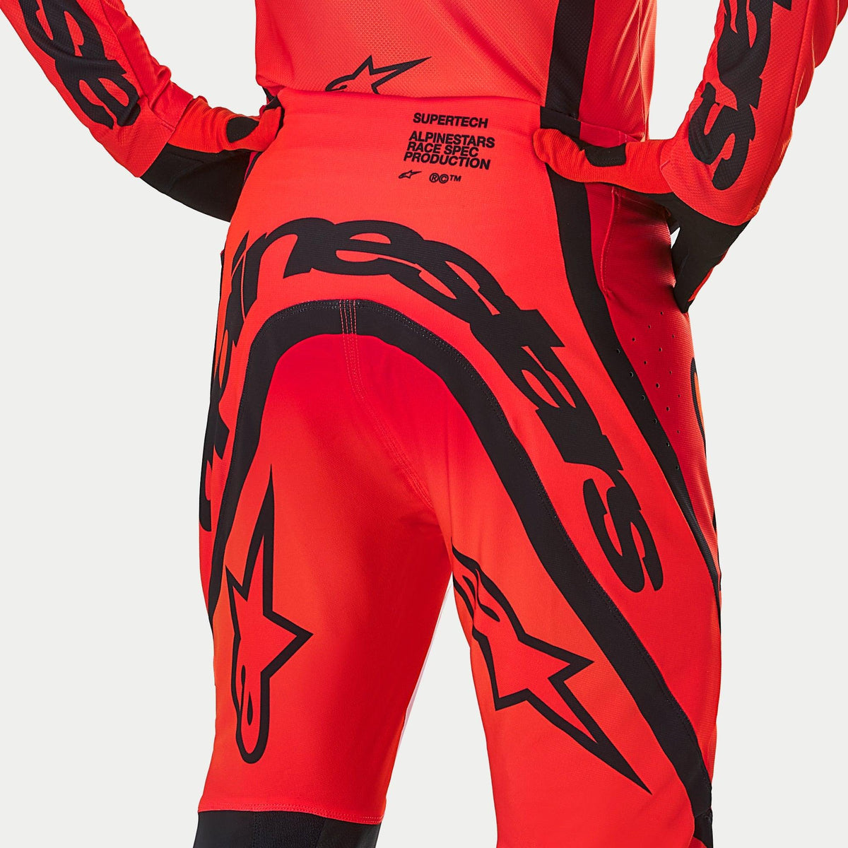 Alpinestars Supertech Ember LE Pants, pantalones de motocross, rojo flúor y rojo brillante con gráficos en negro, vista trasera que resalta el logotipo llamativo y el texto 'Race Spec Production' en la zona lumbar, diseño técnico para competición off-road