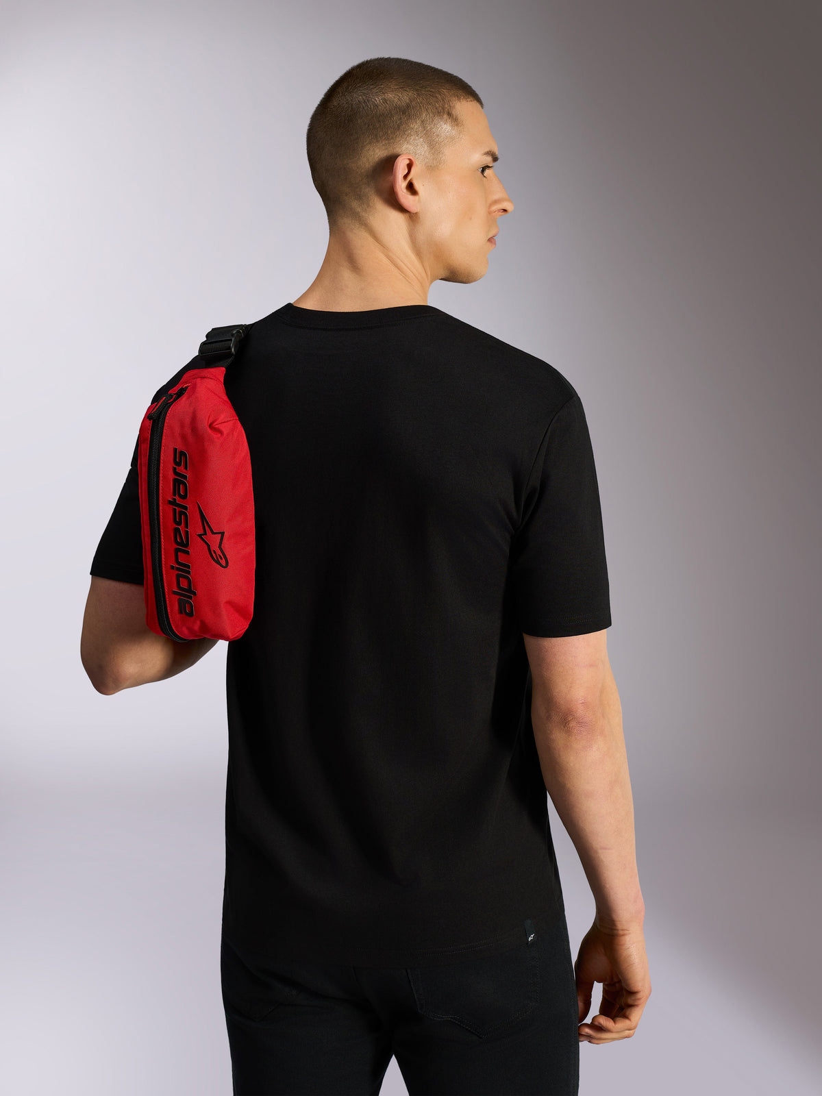 Alpinestars Only Linear Hip Bag, Red and Black, worn over the shoulder as a sling bag by a model in a black t-shirt, featuring vertical zipper and black Alpinestars branding, durable urban accessory.
