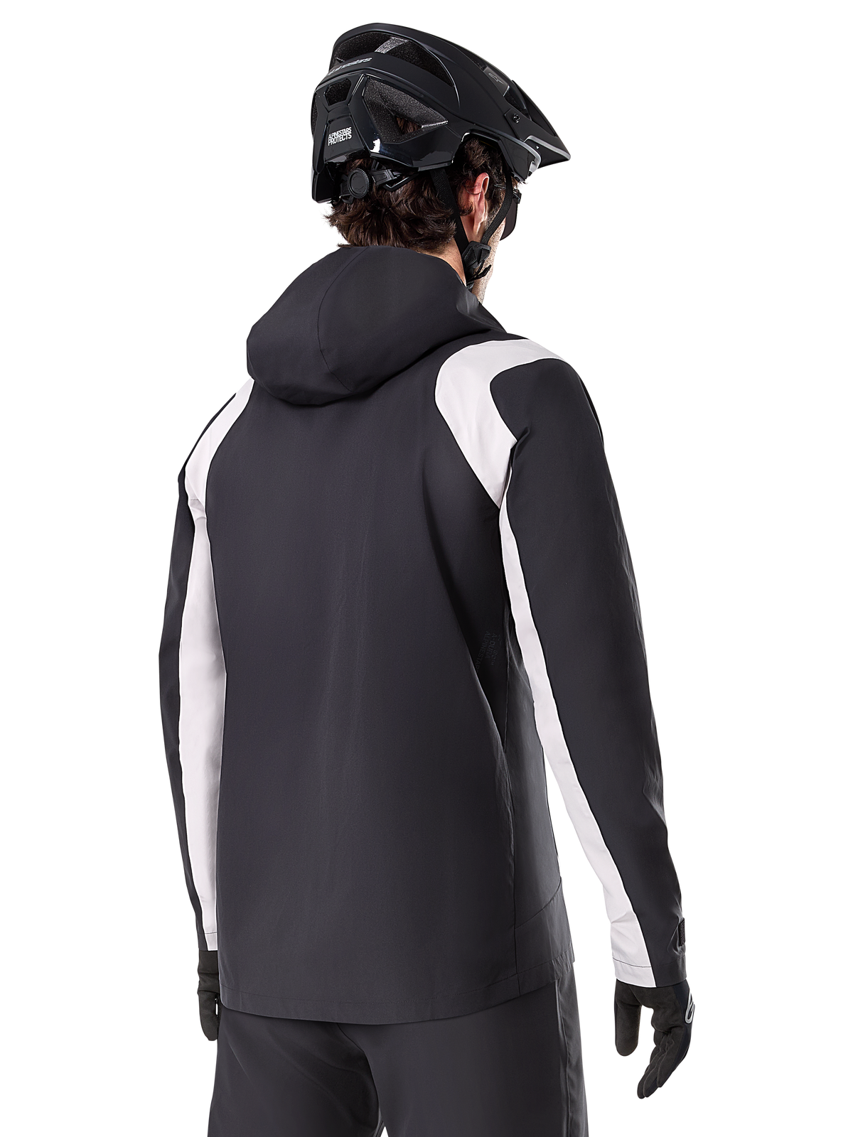Alpinestars A-Dura Rain Jacket, chaqueta impermeable para ciclismo de montaña, negra con paneles blancos en las mangas, vista trasera de un ciclista con casco de MTB y guantes negros, construcción técnica impermeable de 2.5 capas, ropa de ciclismo de montaña