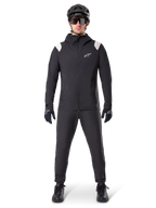 Chaqueta impermeable Alpinestars A-Dura, chaqueta de lluvia para mountain bike, negra con detalles blancos en los hombros y logotipo blanco en el pecho, usada con pantalones negros, casco negro, gafas de sol y guantes, equipamiento de ciclismo de montaña coordinado para clima húmedo.