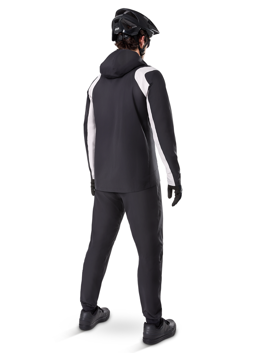 Alpinestars A-Dura Rain Jacket, vista trasera de un ciclista masculino con la chaqueta de MTB impermeable en negro y blanco, pantalones de ciclismo negros a juego, casco negro y guantes, equipamiento técnico para ciclismo de montaña en condiciones húmedas