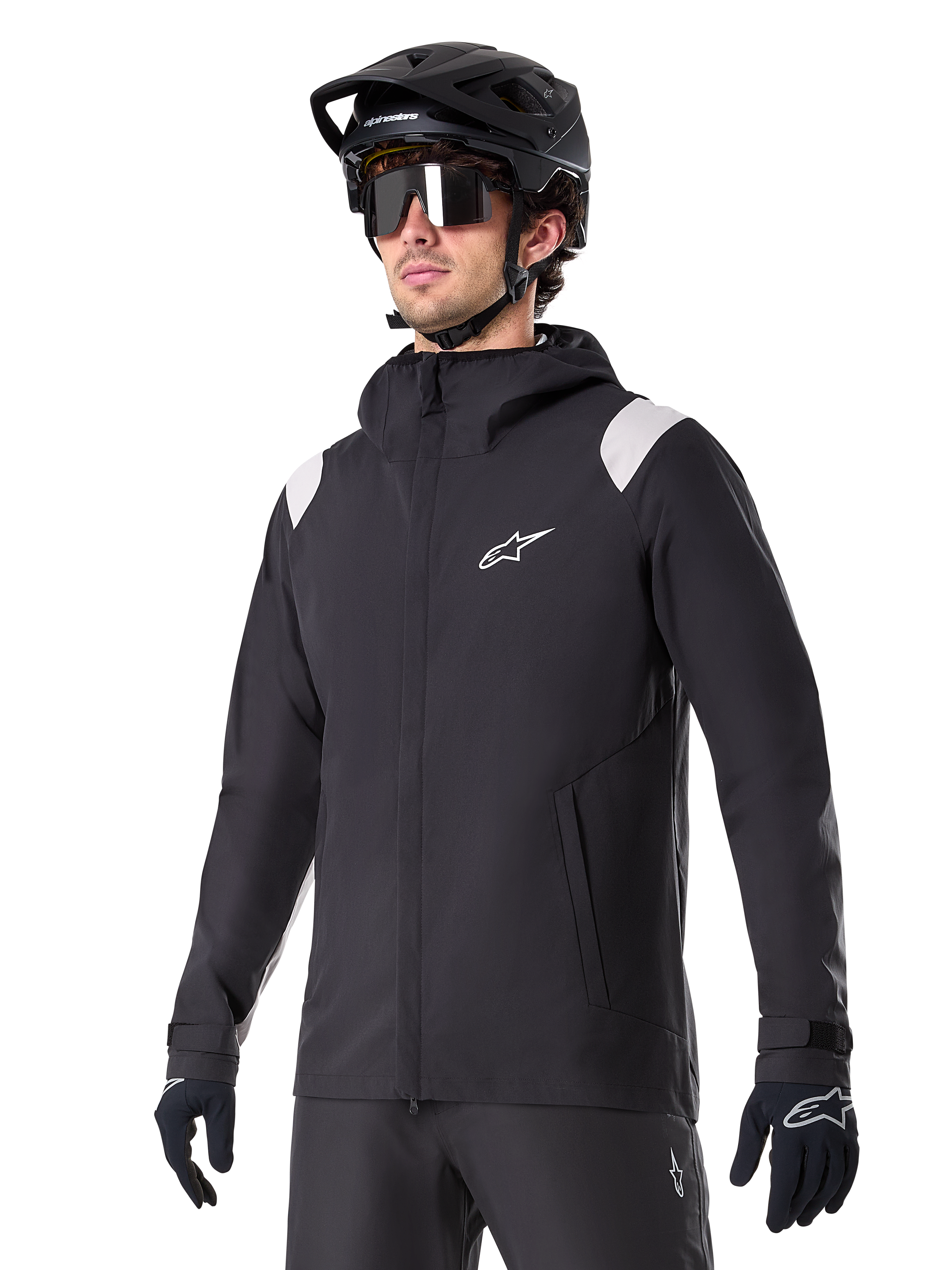Alpinestars A-Dura Rain Jacket, chaqueta de lluvia para mountain bike, negra con detalles en los hombros en gris claro, usada por un ciclista con casco de MTB negro y gafas de sol, logo blanco en el pecho, construcción impermeable, coordinada con pantalones y guantes negros para ciclismo de montaña