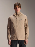 Alpinestars A-Dura Rain Jacket, chaqueta de lluvia con capucha para mountain bike en color marrón claro, usada por un modelo, con un pequeño logotipo en el pecho, correas de puño ajustables y cremallera frontal oculta, equipo de ciclismo impermeable