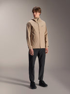 Modelo masculino con la chaqueta de lluvia Alpinestars A-Dura en color marrón claro, combinada con pantalones y calzado negros, chaqueta impermeable minimalista para ciclismo de montaña con diseño de capucha y un pequeño logotipo en el pecho