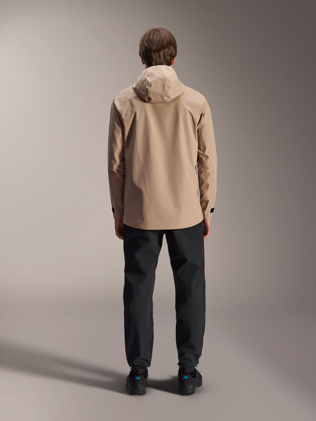 Chaqueta impermeable Alpinestars A-Dura, marrón claro, vista trasera que muestra la capucha y los puños ajustables, combinada con pantalones negros, equipamiento versátil de MTB para todo tipo de clima