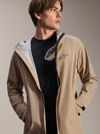 Modelo masculino luciendo la chaqueta impermeable Alpinestars A-Dura, color marrón claro, abierta sobre una camiseta negra, mostrando el forro de malla blanca, chaqueta de ciclismo versátil y resistente a la intemperie