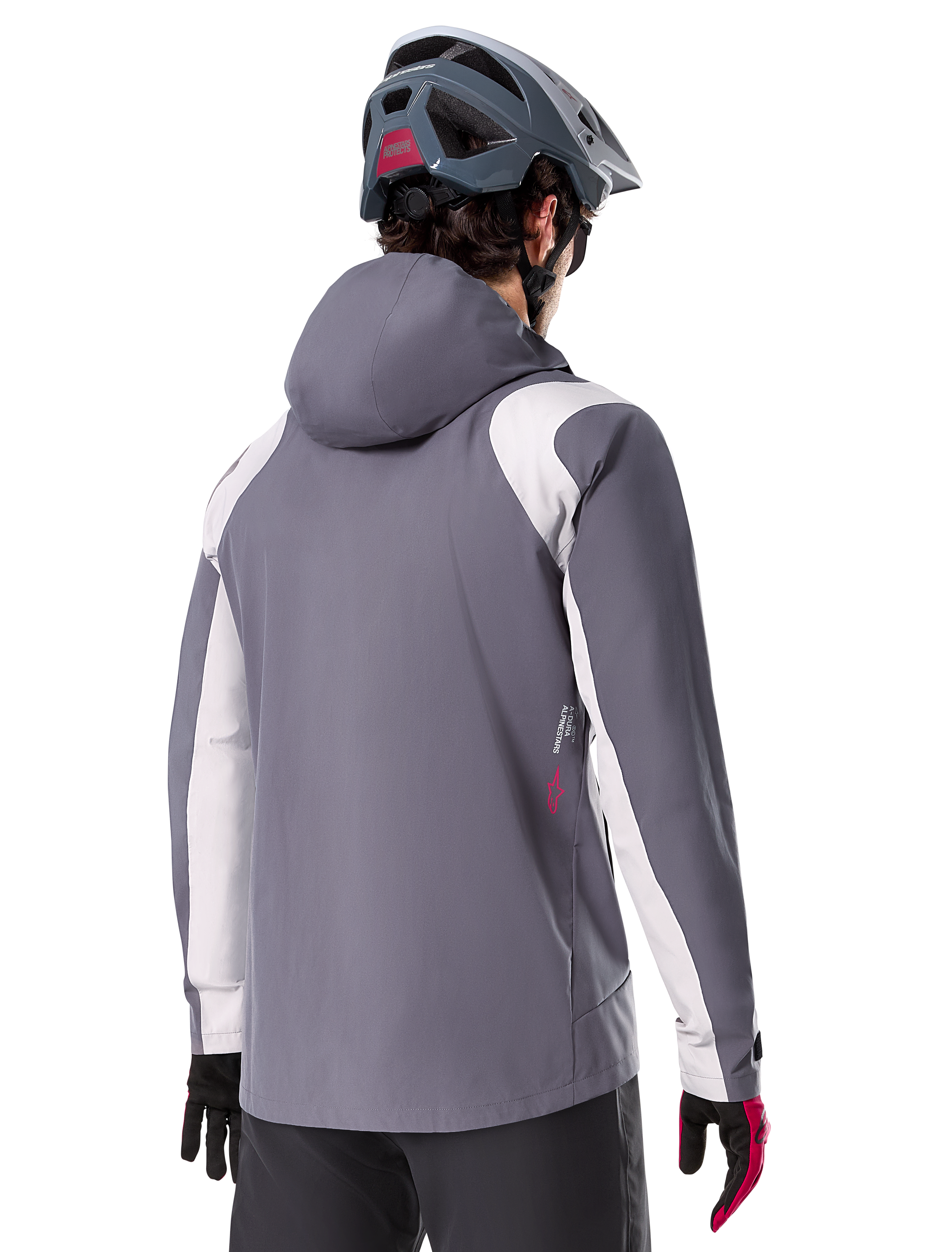 Chaqueta impermeable Alpinestars A-Dura, chaqueta de mountain bike, gris titanio oscuro, vista trasera con paneles en gris claro en hombros y brazos, detalle de logotipo rojo en el lateral, usada con casco de MTB gris y guantes negros y rojos, ropa técnica para ciclismo de montaña