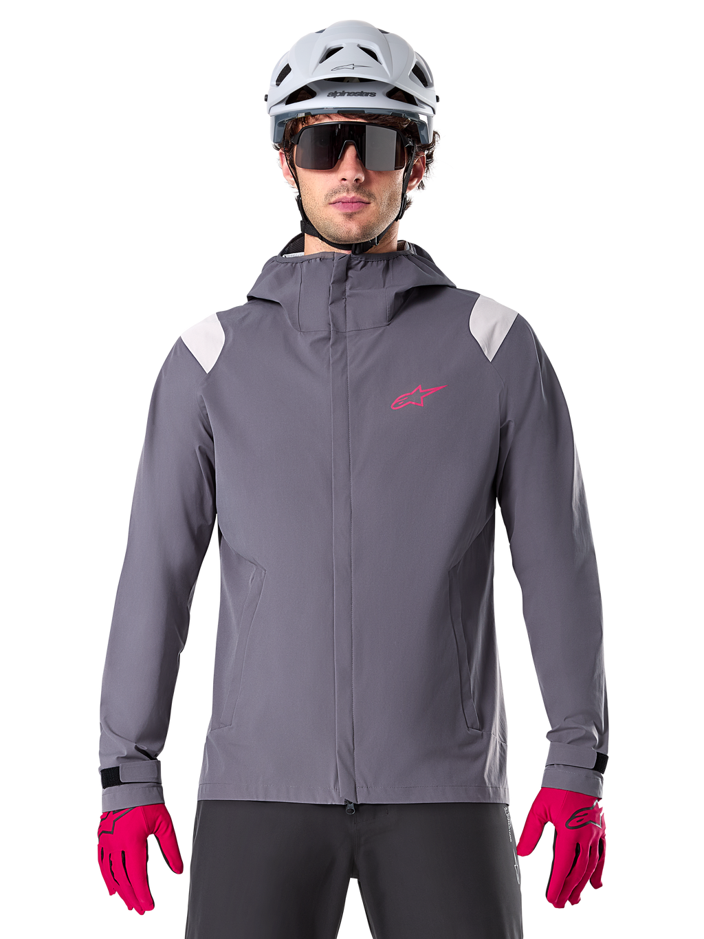 Alpinestars A-Dura Rain Jacket, chaqueta impermeable para ciclismo de montaña, gris titanio oscuro, diseño con capucha con logotipo Alpinestars rosa y paneles gris claro en los hombros, usada con casco de MTB blanco y guantes rosa brillante, equipamiento impermeable para ciclismo todoterreno