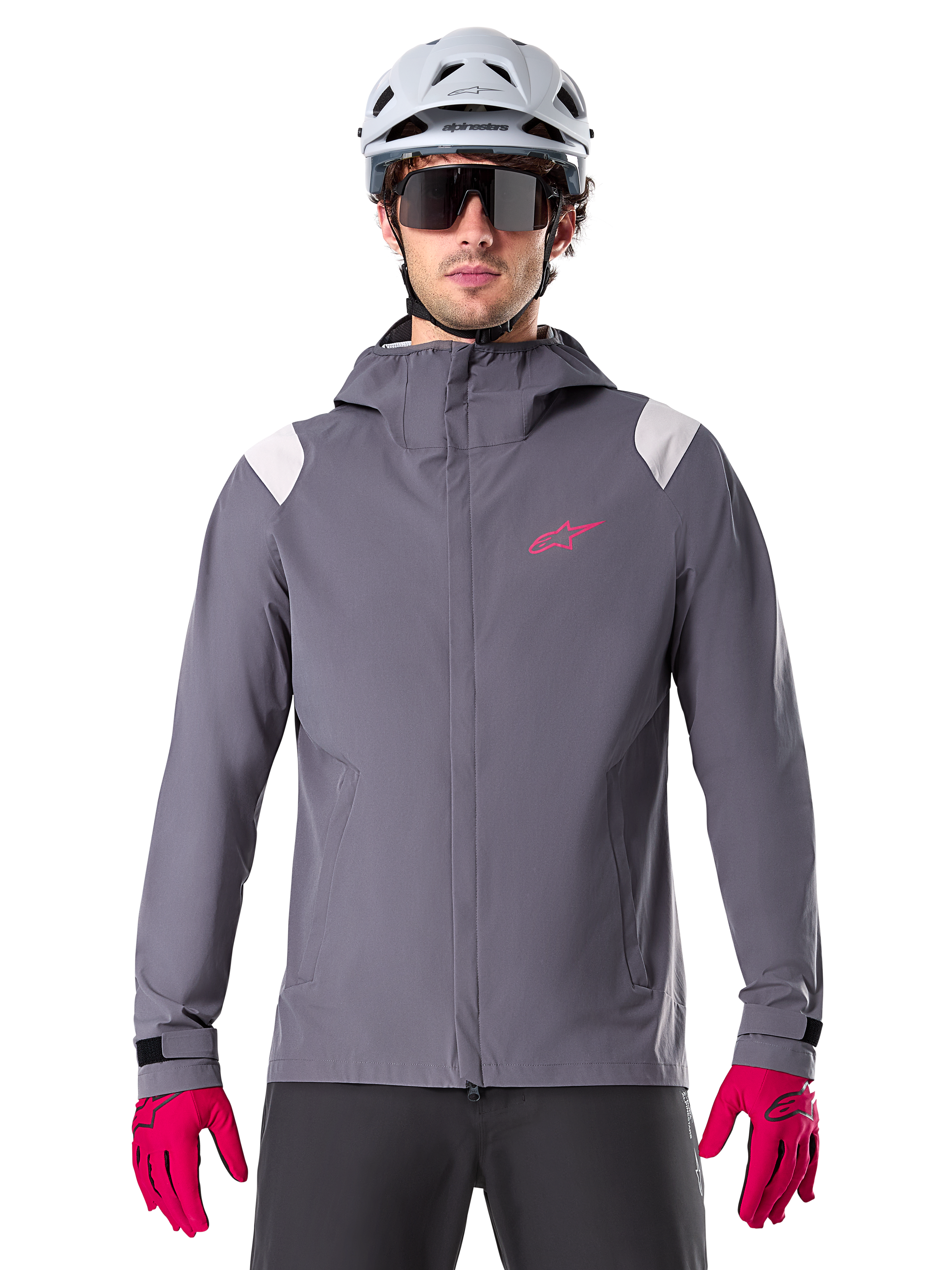 Alpinestars A-Dura Rain Jacket, chaqueta impermeable para ciclismo de montaña, gris titanio oscuro, diseño con capucha con logotipo Alpinestars rosa y paneles gris claro en los hombros, usada con casco de MTB blanco y guantes rosa brillante, equipamiento impermeable para ciclismo todoterreno