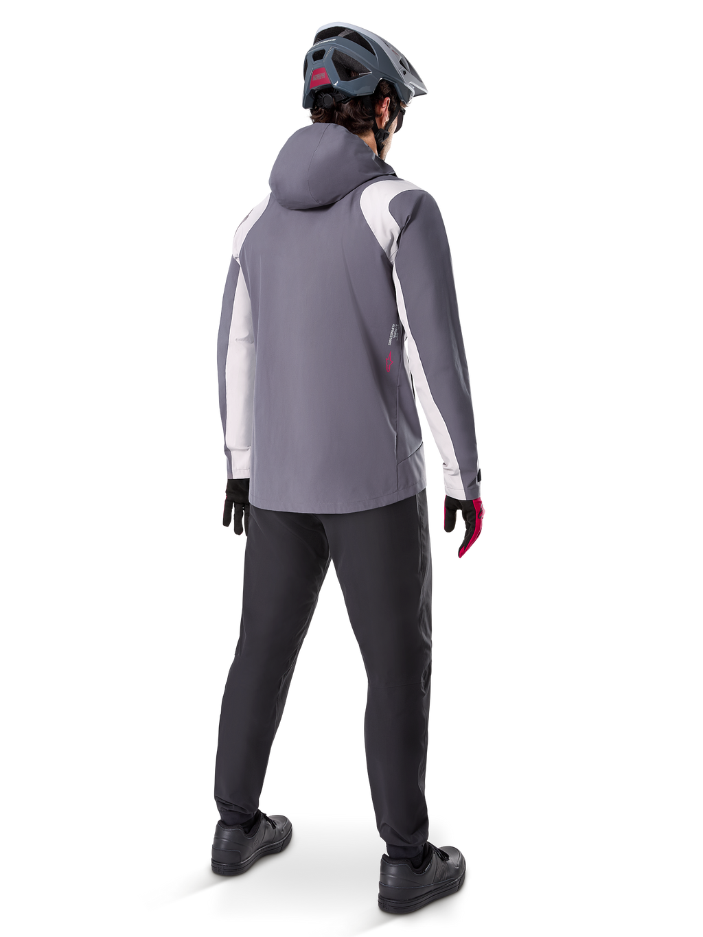 Alpinestars A-Dura Rain Jacket, chaqueta de ciclismo de montaña, gris titanio oscuro con paneles blancos, vista trasera de un ciclista con casco gris a juego y pantalones negros, equipamiento técnico para climas húmedos