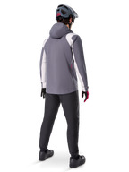 Alpinestars A-Dura Rain Jacket, chaqueta de ciclismo de montaña, gris titanio oscuro con paneles blancos, vista trasera de un ciclista con casco gris a juego y pantalones negros, equipamiento técnico para climas húmedos
